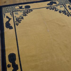 Golden-tan low-pile rug with navy and light blue geometric borders rests on rustic wood planks.