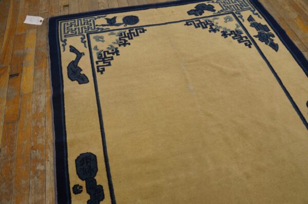 Golden-tan low-pile rug with navy and light blue geometric borders rests on rustic wood planks.