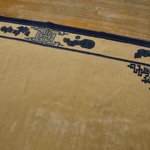 A light tan rug with a navy blue border featuring geometric and abstract motifs sits on a distressed wood floor.