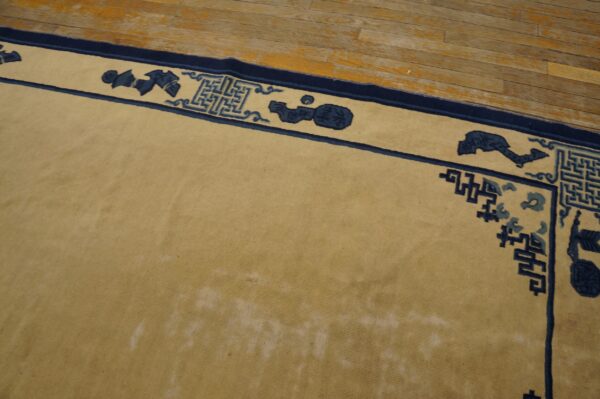 A light tan rug with a navy blue border featuring geometric and abstract motifs sits on a distressed wood floor.