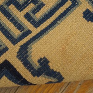 Close view of a tan and two-tone blue geometric maze pattern rug lying on wood floor.