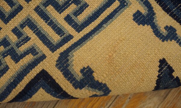 Close view of a tan and two-tone blue geometric maze pattern rug lying on wood floor.