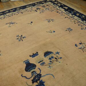 Tan rug with scattered navy and light blue botanical designs and a complex border on wood flooring.