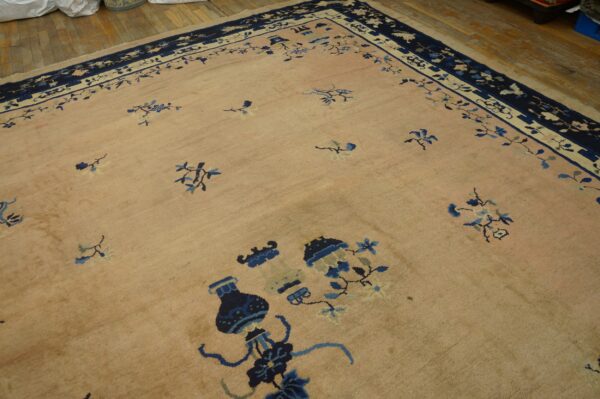Tan rug with scattered navy and light blue botanical designs and a complex border on wood flooring.