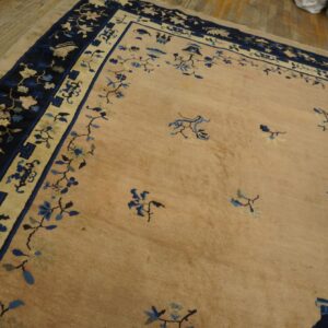 Tan rug with scattered blue floral motifs and a wide navy border on light wooden floorboards.