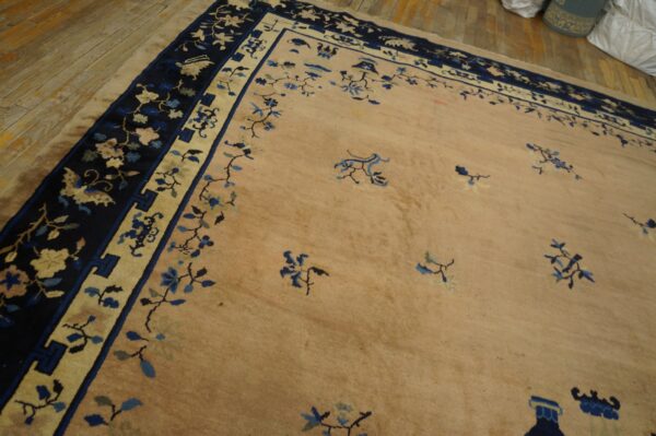 Tan rug with scattered blue floral motifs and a wide navy border on light wooden floorboards.