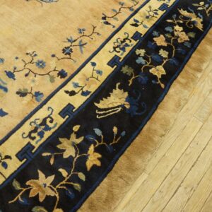 Tan and deep blue floral rug border with medium pile rests on light-colored wood plank flooring.