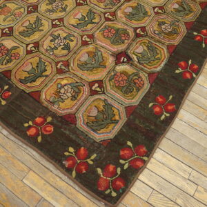 Textured rug corner showing a hexagonal gold pattern with red and green florals resting on distressed wooden floors.