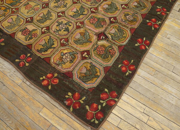 Textured rug corner showing a hexagonal gold pattern with red and green florals resting on distressed wooden floors.