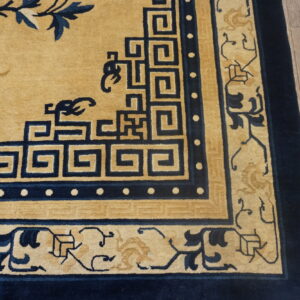 This rug features a tan field, navy blue fretwork, and detailed floral borders on distressed wooden planks.