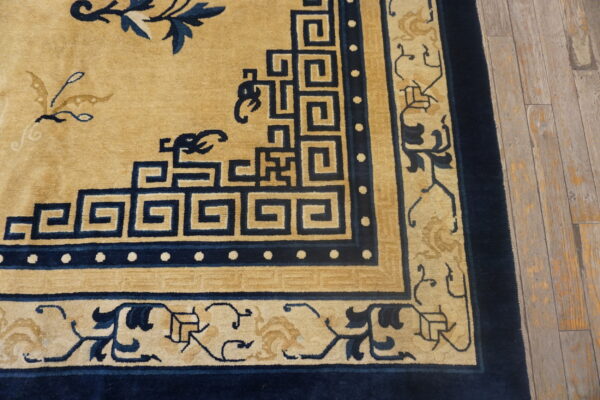 This rug features a tan field, navy blue fretwork, and detailed floral borders on distressed wooden planks.