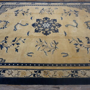 Low-pile golden tan rug with intricate navy blue geometric borders and scattered floral motifs on a wood floor.