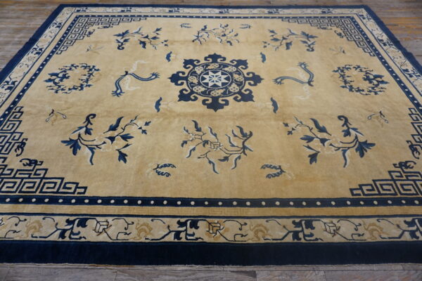 Low-pile golden tan rug with intricate navy blue geometric borders and scattered floral motifs on a wood floor.