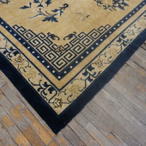 Tan rug with complex navy blue geometric and floral borders sits atop distressed gray wood flooring.