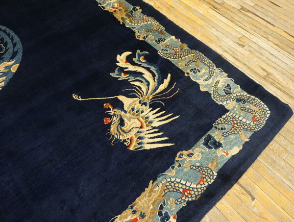 Detailed navy rug with beige and teal dragon and bird motifs on light plank wood floors.