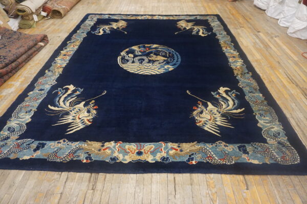 Large navy rug with beige and pale blue dragon and phoenix motifs lies on wood plank flooring.