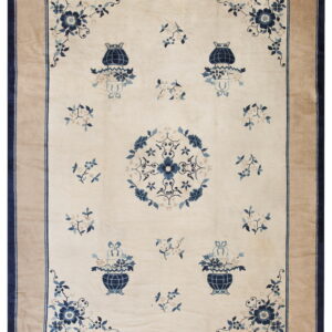 Cream and blue floral rug with a central medallion, stylized urns, and a wide solid tan border.