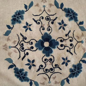 Textured cream rug with a centered floral medallion pattern in navy, light blue, and taupe colors.