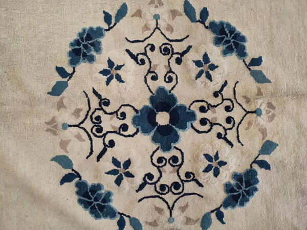 Textured cream rug with a centered floral medallion pattern in navy, light blue, and taupe colors.