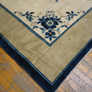 Beige rug corner featuring blue floral designs, a wide tan border, and dark blue trim on plank hardwood.
