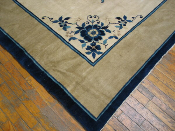 Beige rug corner featuring blue floral designs, a wide tan border, and dark blue trim on plank hardwood.