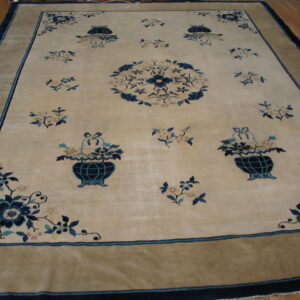 Large pale tan rug with navy blue floral sprays, a center medallion, and a wide khaki border on hardwood.