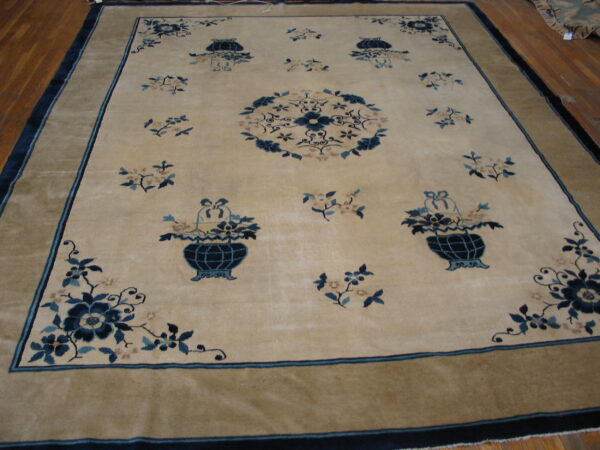 Large pale tan rug with navy blue floral sprays, a center medallion, and a wide khaki border on hardwood.