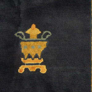 Dark blue rug featuring a golden stylized vase design next to an ornate yellow and blue border.
