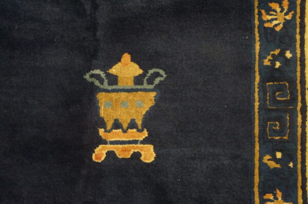 Dark blue rug featuring a golden stylized vase design next to an ornate yellow and blue border.