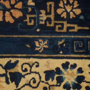 Dark blue rug detail featuring stylized gold and rust-colored floral patterns with linear geometric borders.