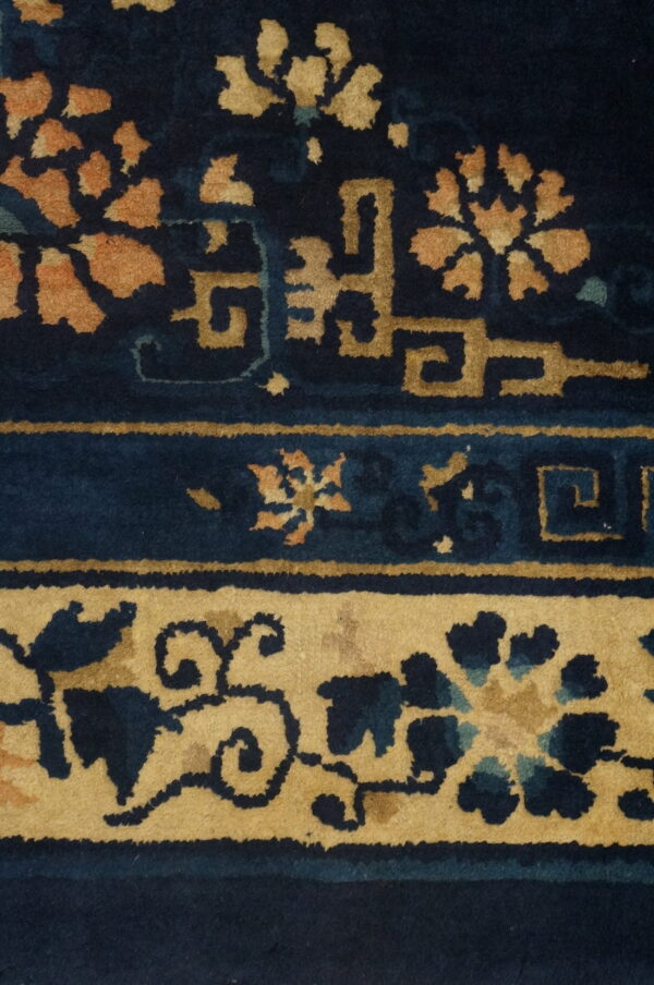 Dark blue rug detail featuring stylized gold and rust-colored floral patterns with linear geometric borders.