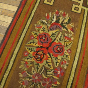 Brown runner rug with a bright red, olive, and green floral motif on worn plank wood flooring.