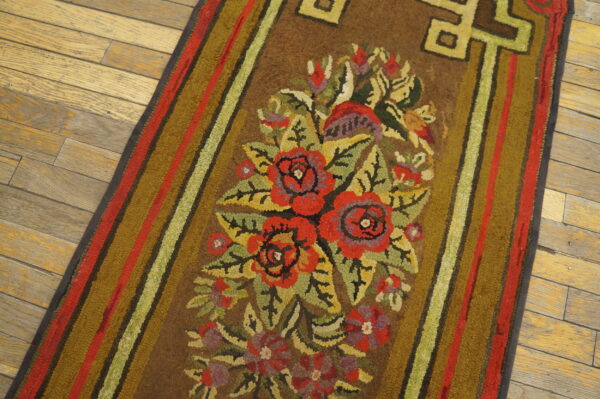 Brown runner rug with a bright red, olive, and green floral motif on worn plank wood flooring.