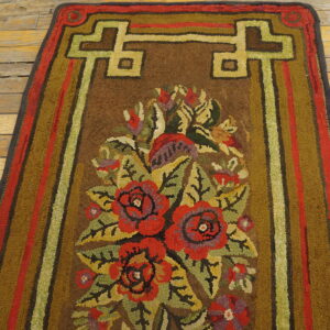 Brown hook-pile runner rug with colorful floral motifs and green geometric borders on worn wood planks.