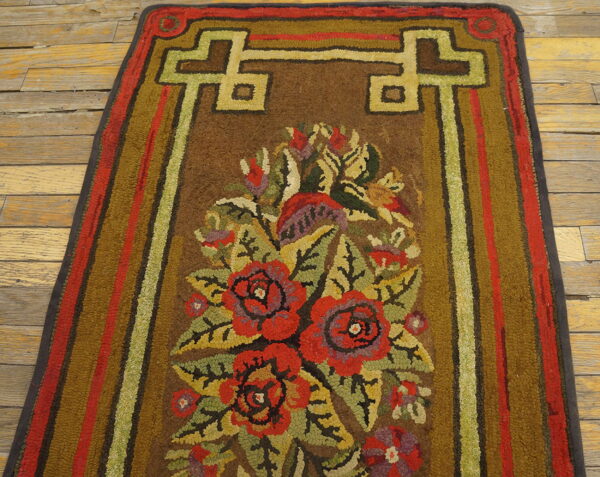 Brown hook-pile runner rug with colorful floral motifs and green geometric borders on worn wood planks.