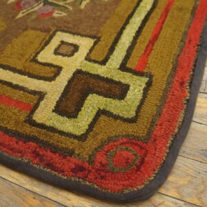 Close-up of a textured rug corner with brown, red, green, and yellow geometric designs on distressed wood.