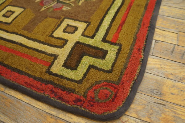 Close-up of a textured rug corner with brown, red, green, and yellow geometric designs on distressed wood.