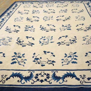 Cream and indigo rug featuring a repeating vine pattern and complex borders resting on hardwood flooring.