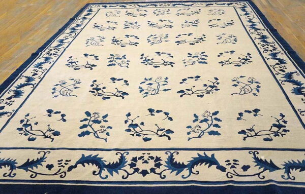 Cream and indigo rug featuring a repeating vine pattern and complex borders resting on hardwood flooring.