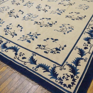 Low-pile cream and navy rug with floral motifs and wide decorative borders on wood planks.