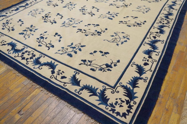 Low-pile cream and navy rug with floral motifs and wide decorative borders on wood planks.