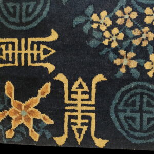 Detail of a navy blue low-pile rug patterned with gold stylized symbols, teal medallions, and yellow flowers.