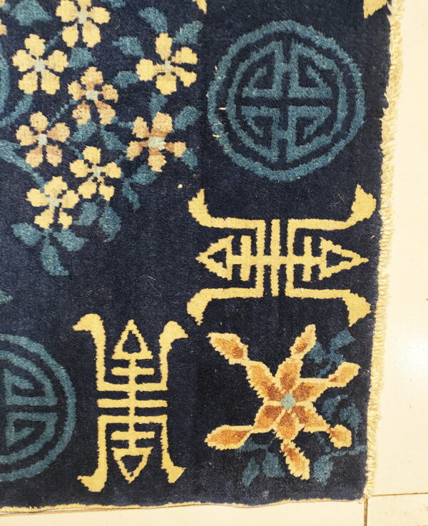 Deep pile navy rug featuring yellow floral sprays, teal symbols, and gold characters on a light tile floor.