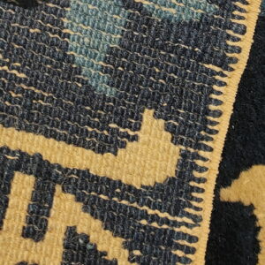 Close-up of a gold and dark blue geometric flatweave pattern beside a solid high-pile section.