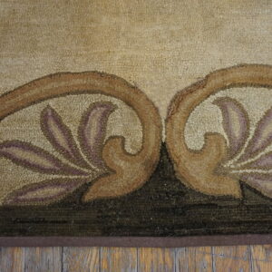 Beige, brown, and mauve floral motif detail on a textured area rug placed on distressed wood flooring.