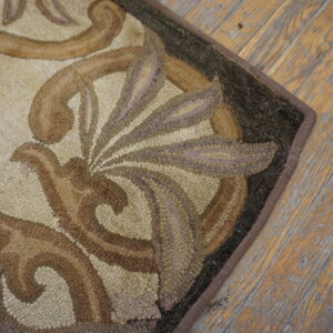 A textured rug edge with brown and beige baroque designs rests on worn hardwood floorboards.