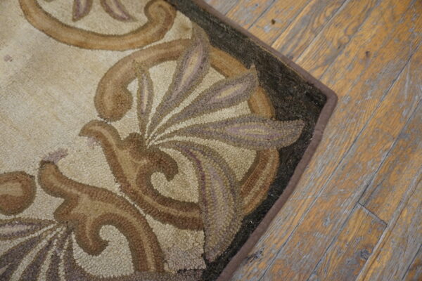 A textured rug edge with brown and beige baroque designs rests on worn hardwood floorboards.