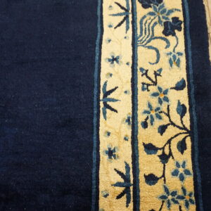 A close-up view of a navy rug field next to a tan and blue floral border on light wood flooring.