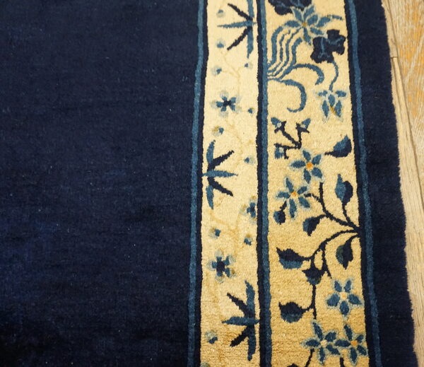 A close-up view of a navy rug field next to a tan and blue floral border on light wood flooring.