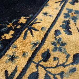 Close-up view of plush rug pile in dark navy and tan with intricate blue and gold floral patterns.